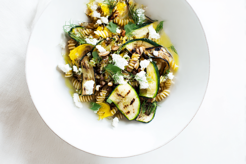 Person drizzling extra virgin olive oil over roasted vegetables